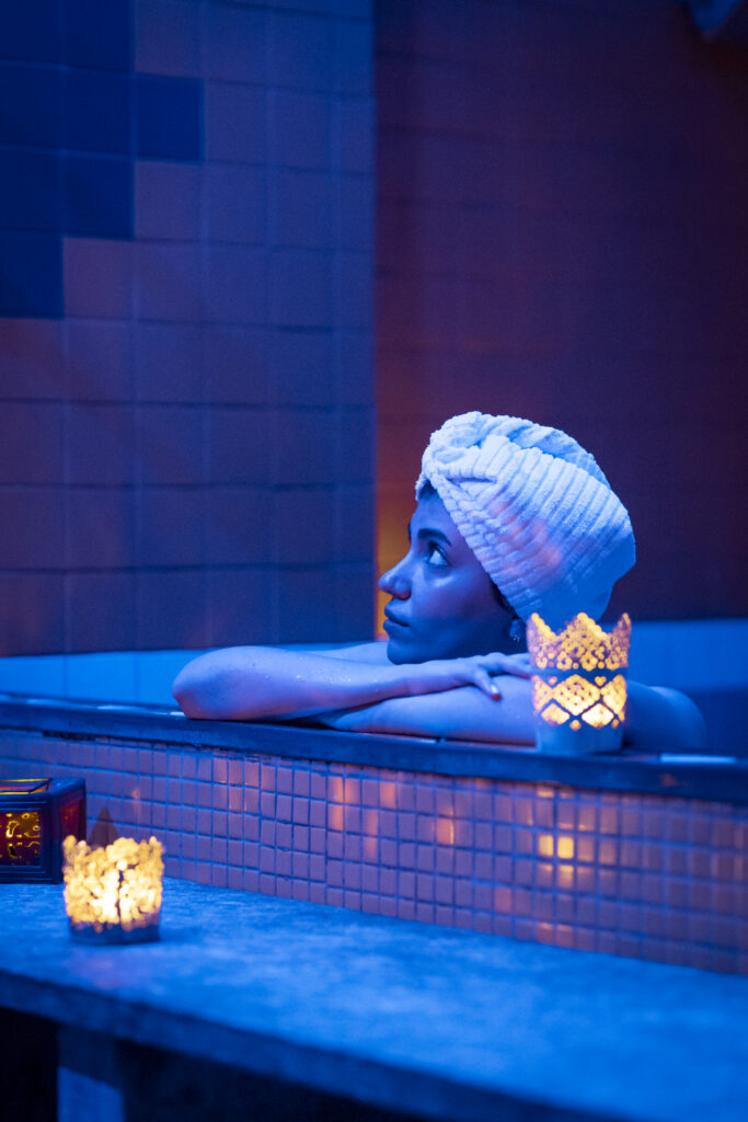 Donna con il turbante di spugna appoggiata al bordo della vasca dell'hammam tra le lanterne